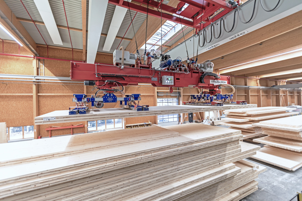 Two suction spiders on an overhead crane stack the cross-laminated timber panels until they are ready for further use.